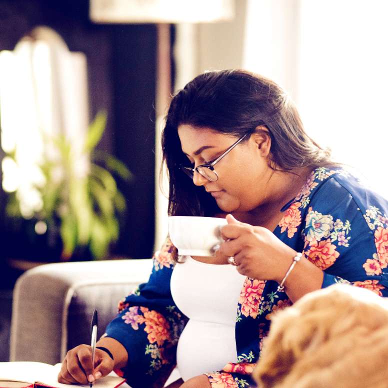 Woman writing in a notebook and holding a tea cup