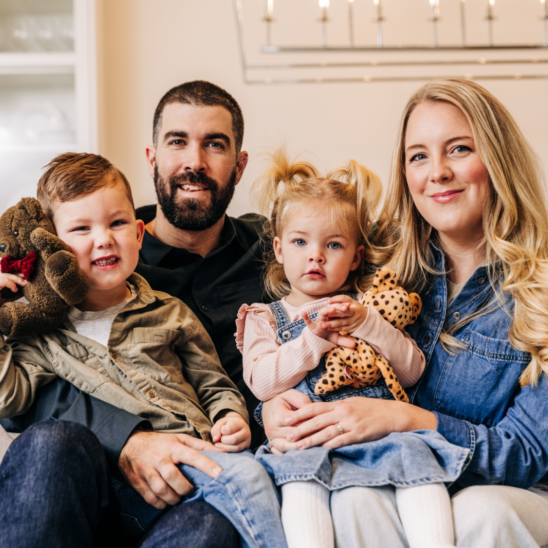 A mother, father, and two young children smiling while sitting inside their home