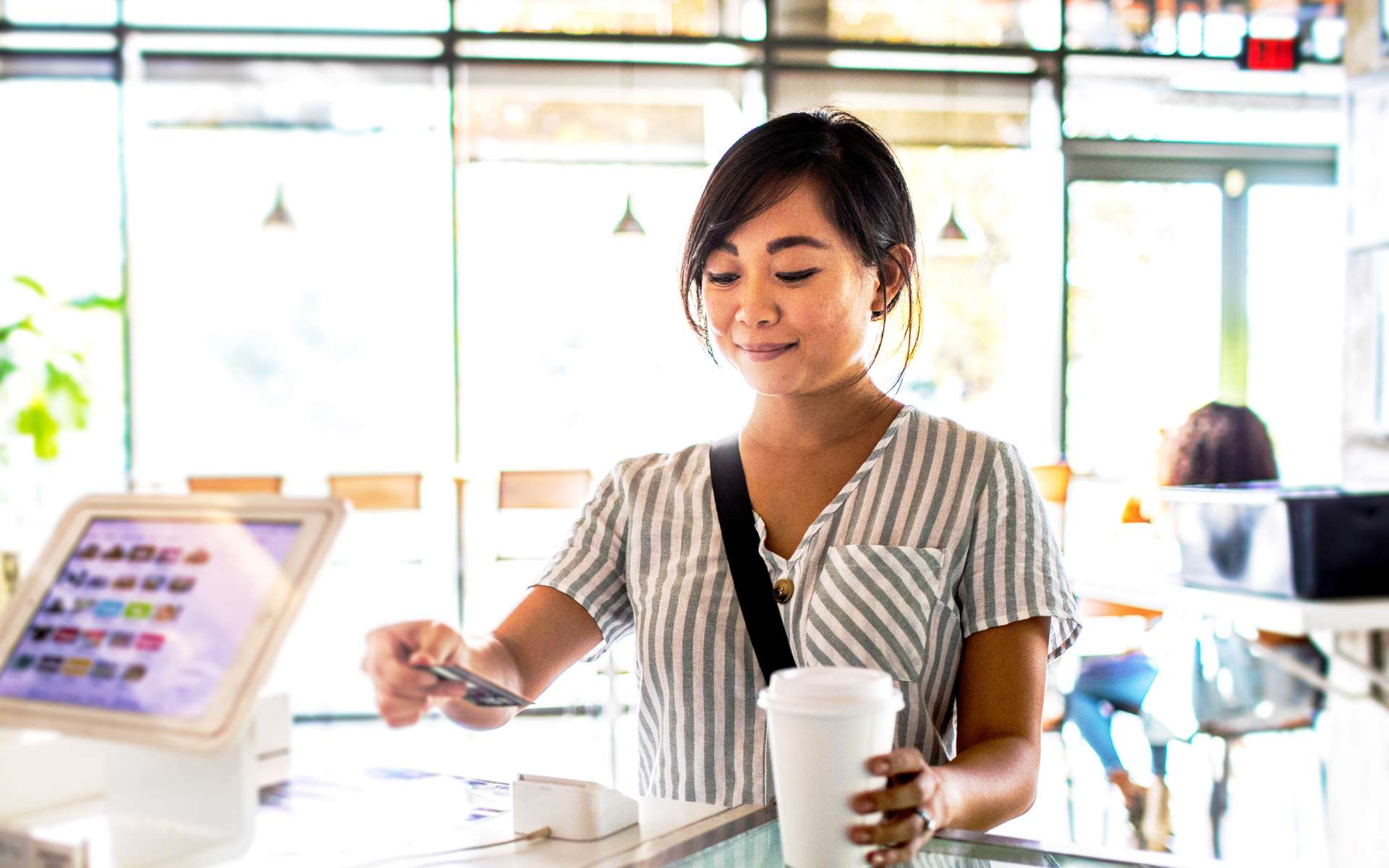 A woman pays for her coffee by tapping her debit card