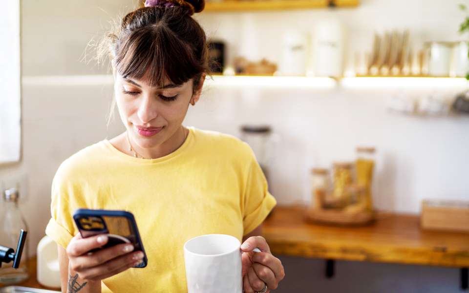 A young woman is looking at her phone, holding a coffee cup