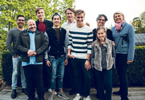 A diverse group of nine people - young and old - are smiling on a deck outside.