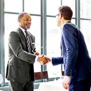 An older black man and a young white man with glasses shake hands over a desk.