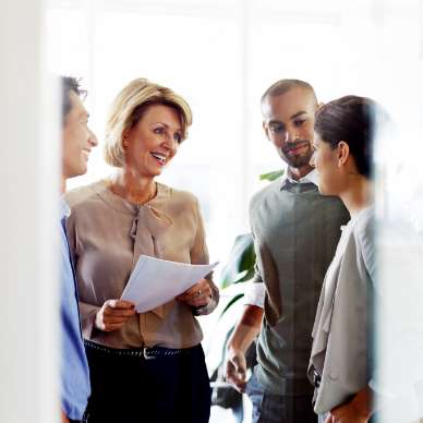 A diverse group, seen through a door, smiles and chats together.