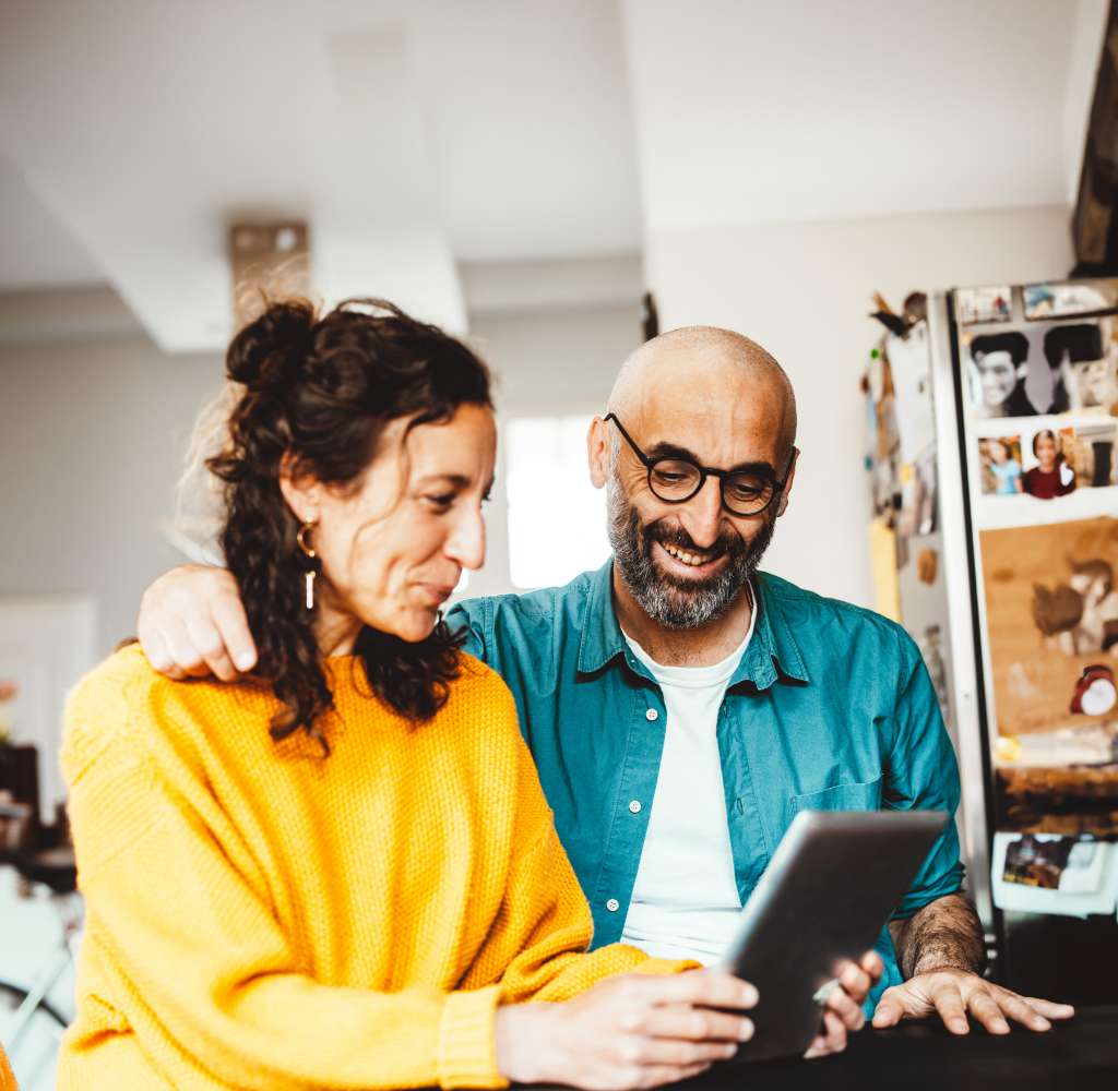 Mid age couple happily sitting close together and look at a tablet