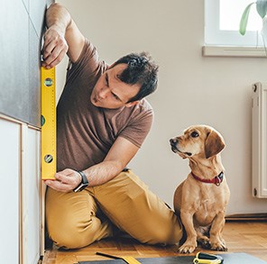 man doing home improvements using a level while dog watches