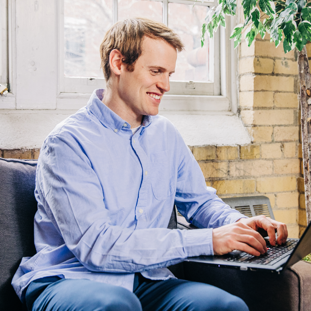 Light skinned man using his laptop while smiling.