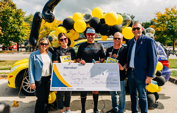 A group of Meridian employees holding a cheque at an outdoor event with balloons and trees in the distance. 