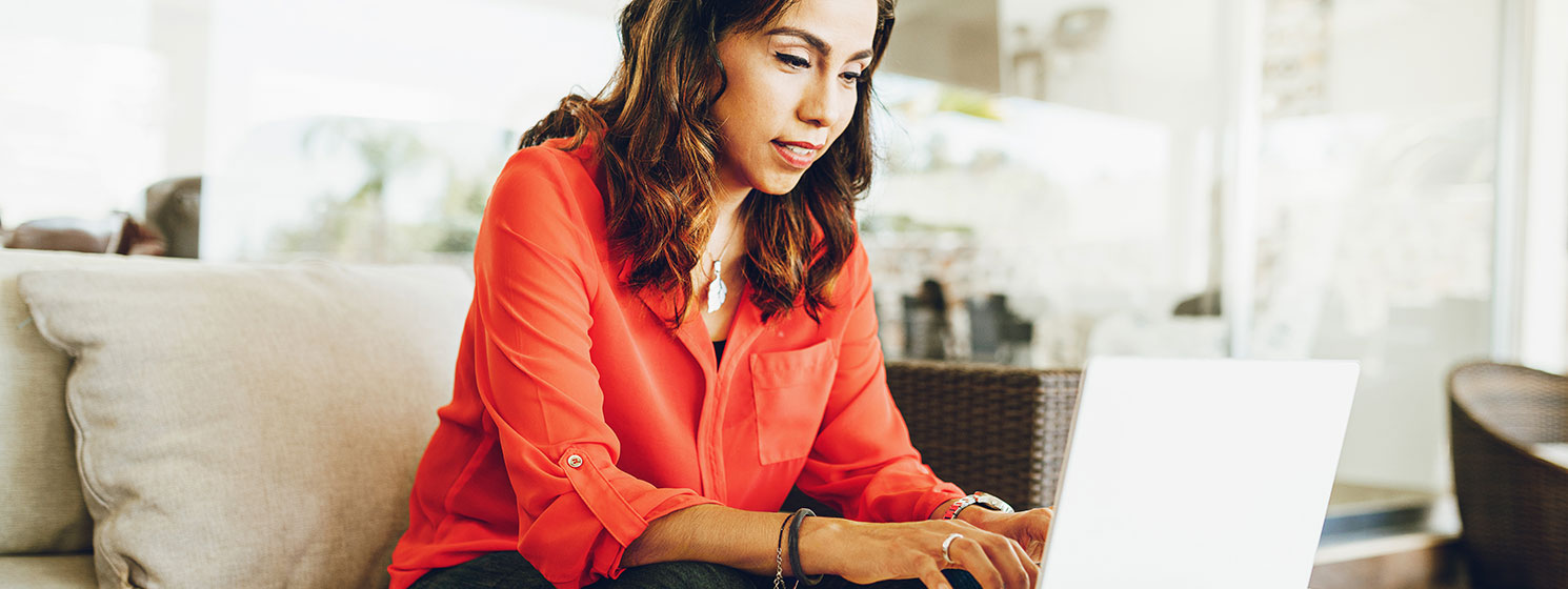 Woman with dark hair and medium skin tone works on a laptop in her living room.