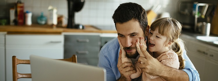 Father and young daughter in the kitchen on a laptop together.