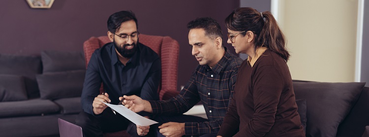 A couple sit on a couch reviewing documents with an advisor.