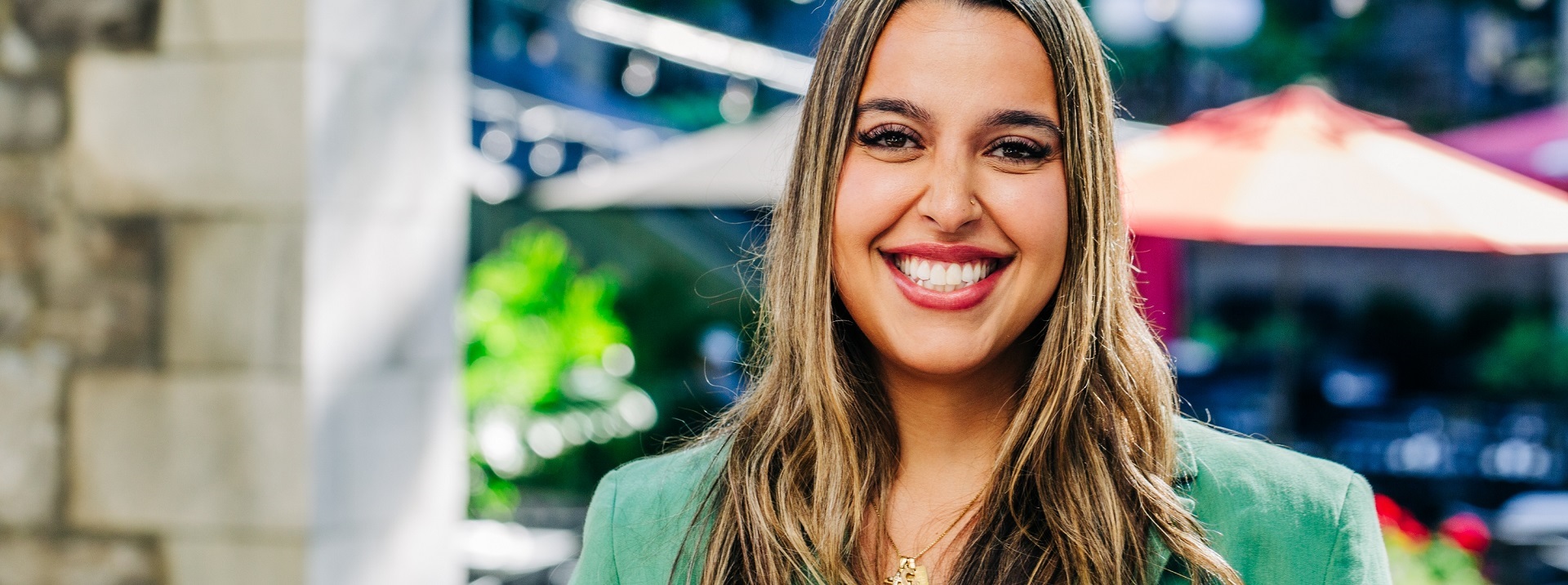 A smiling woman standing outside, dressed in a green blazer.