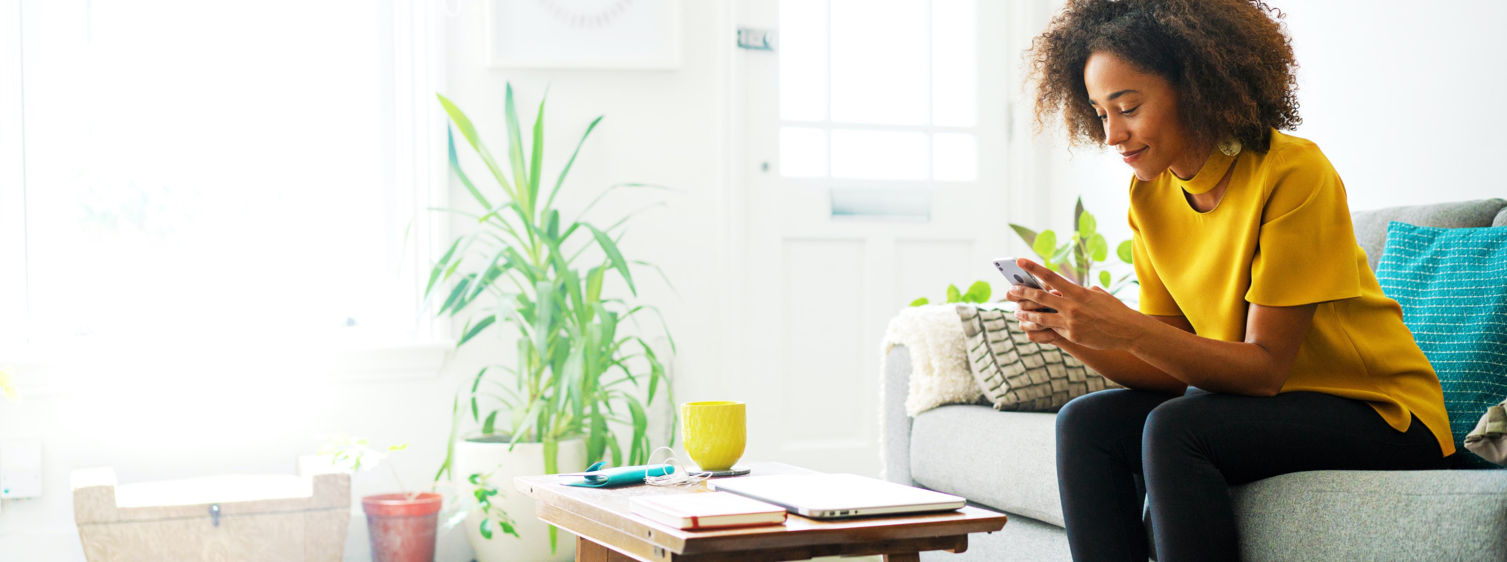 woman sitting on couch in her sunny living room looking at her phone