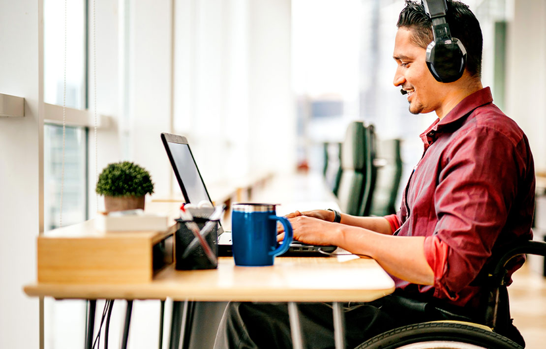 a man sitting on a wheelchair with his headphones working on a laptop