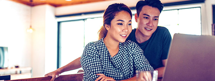 Young couple at home, looking interested in something on a desktop computer