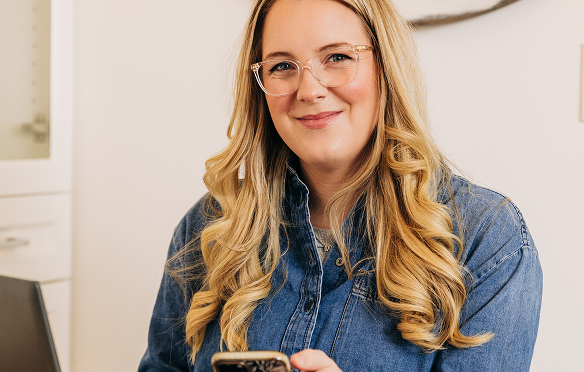 Young woman with long blond hair smiles holding her phone