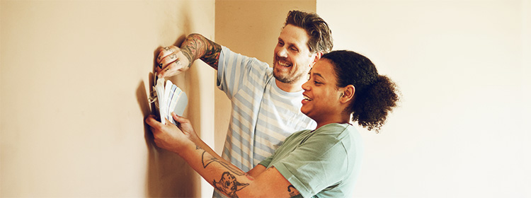 Smiling young couple compare paint samples on a wall