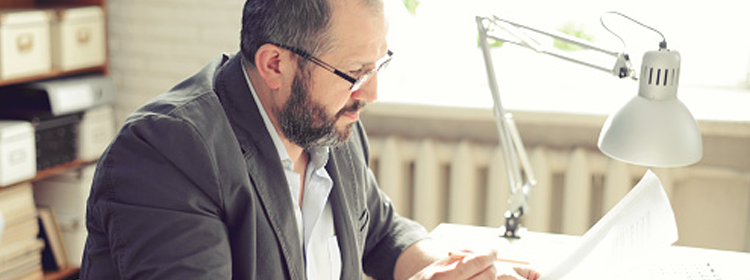 Middle aged man in a suit sits in an office reviewing documents.