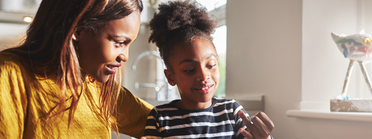 A black woman and her daughter sit together in the kitchen.