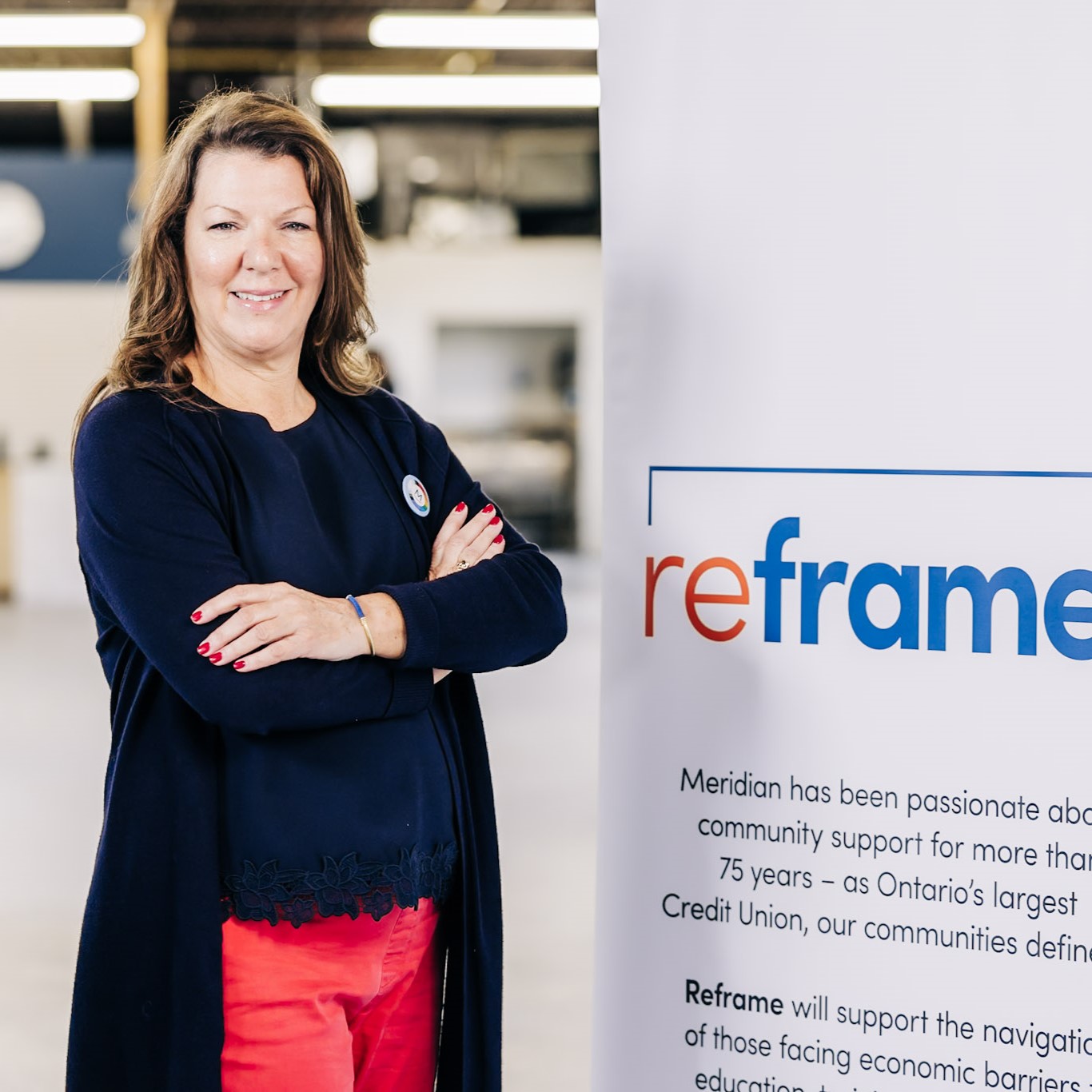 Light skinned woman with shoulder-length hair, smiles with arms crossed, standing next to a Reframe poster. 