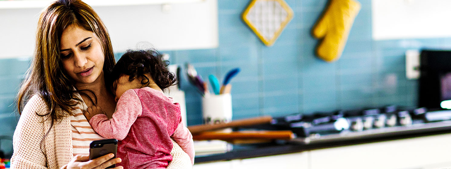 Concerned Mother holding her baby while multi-tasking on cellphone