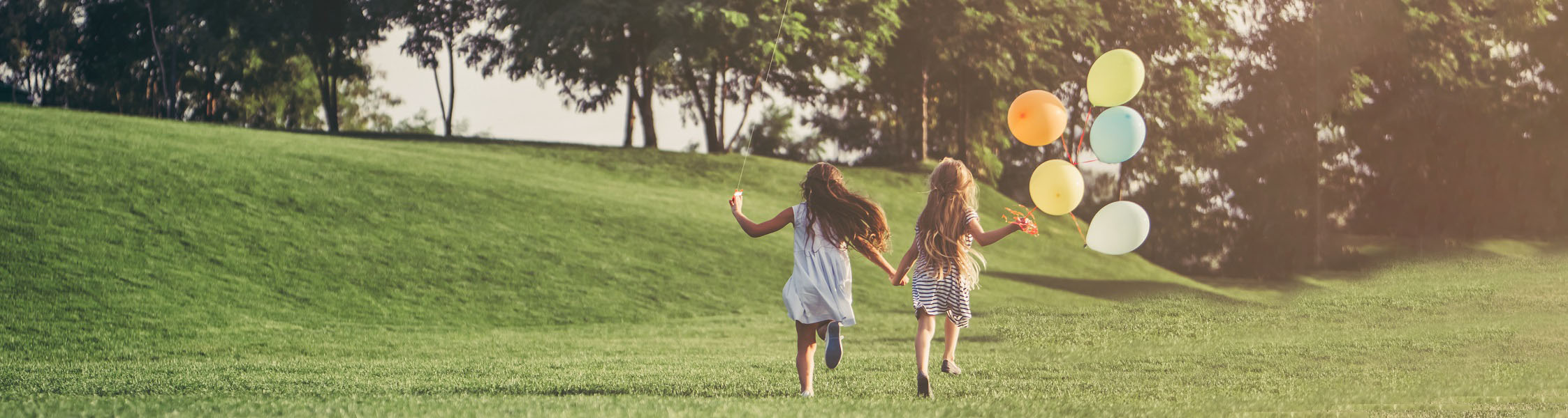 Two young girls running across grass and holding balloons