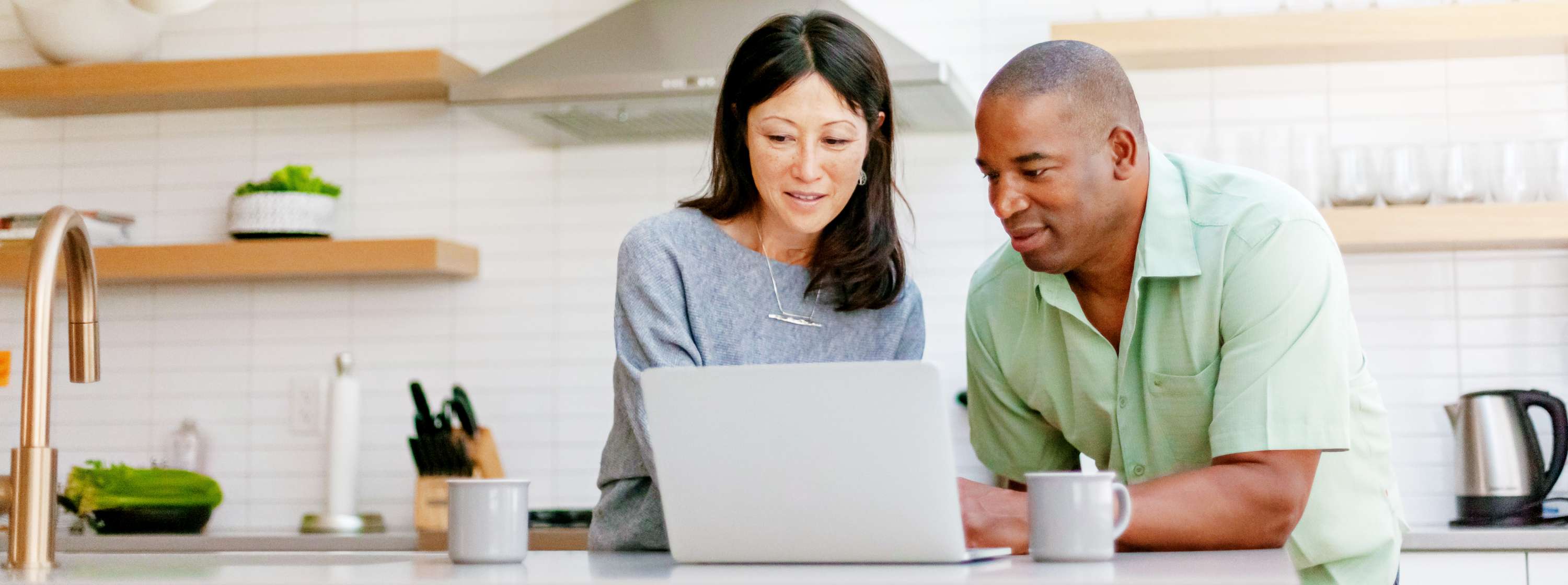 Mixed race couple in their kitchen, looking at a computer