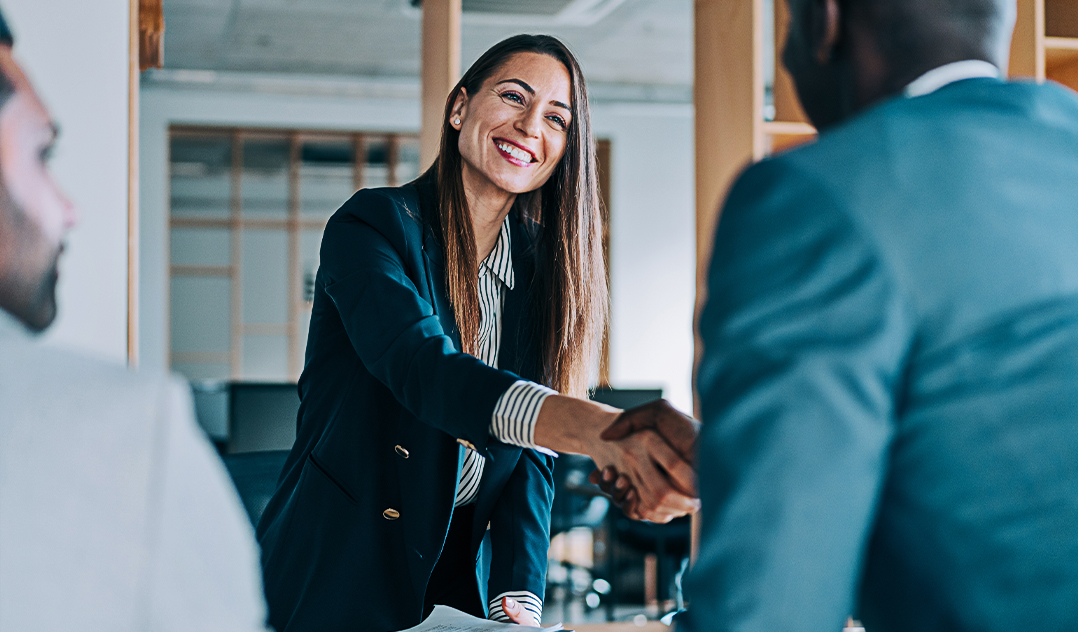 A female advisor, smiles and shakes hands with her client