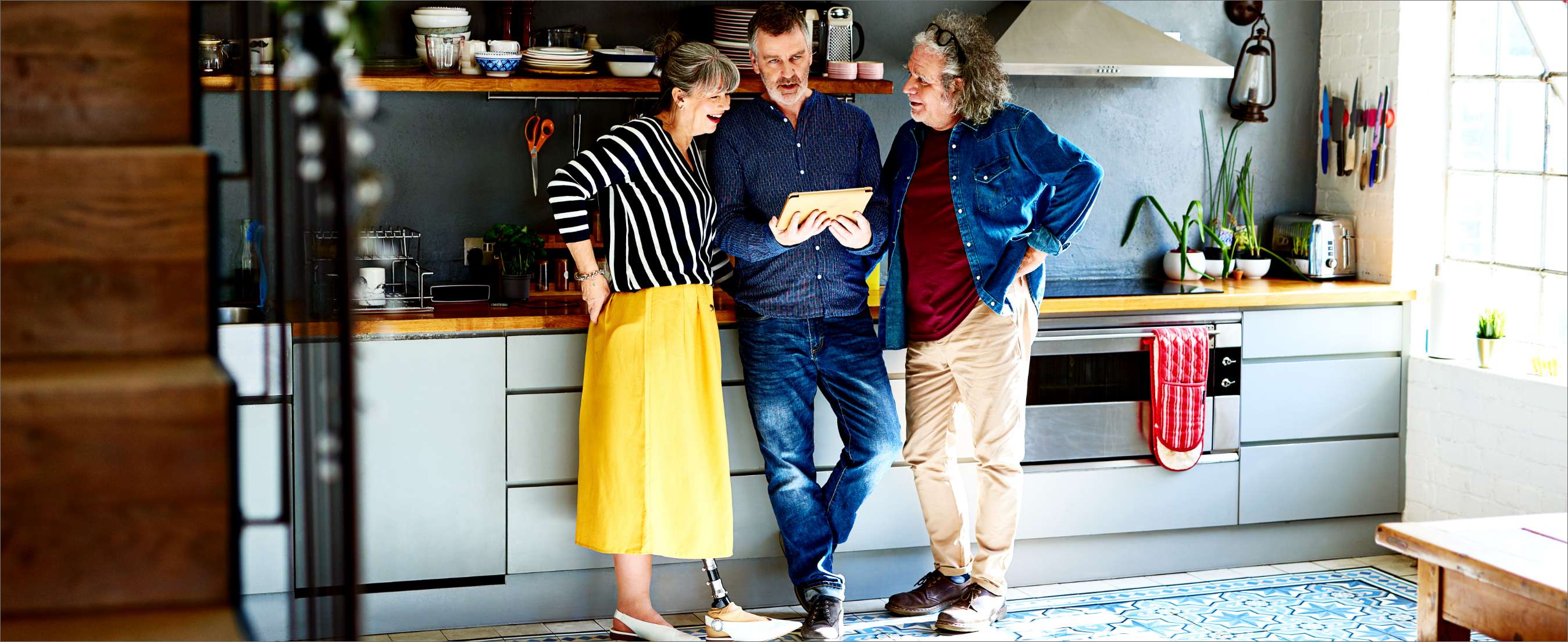 Three mature friends with tablet discussing in the kitchen