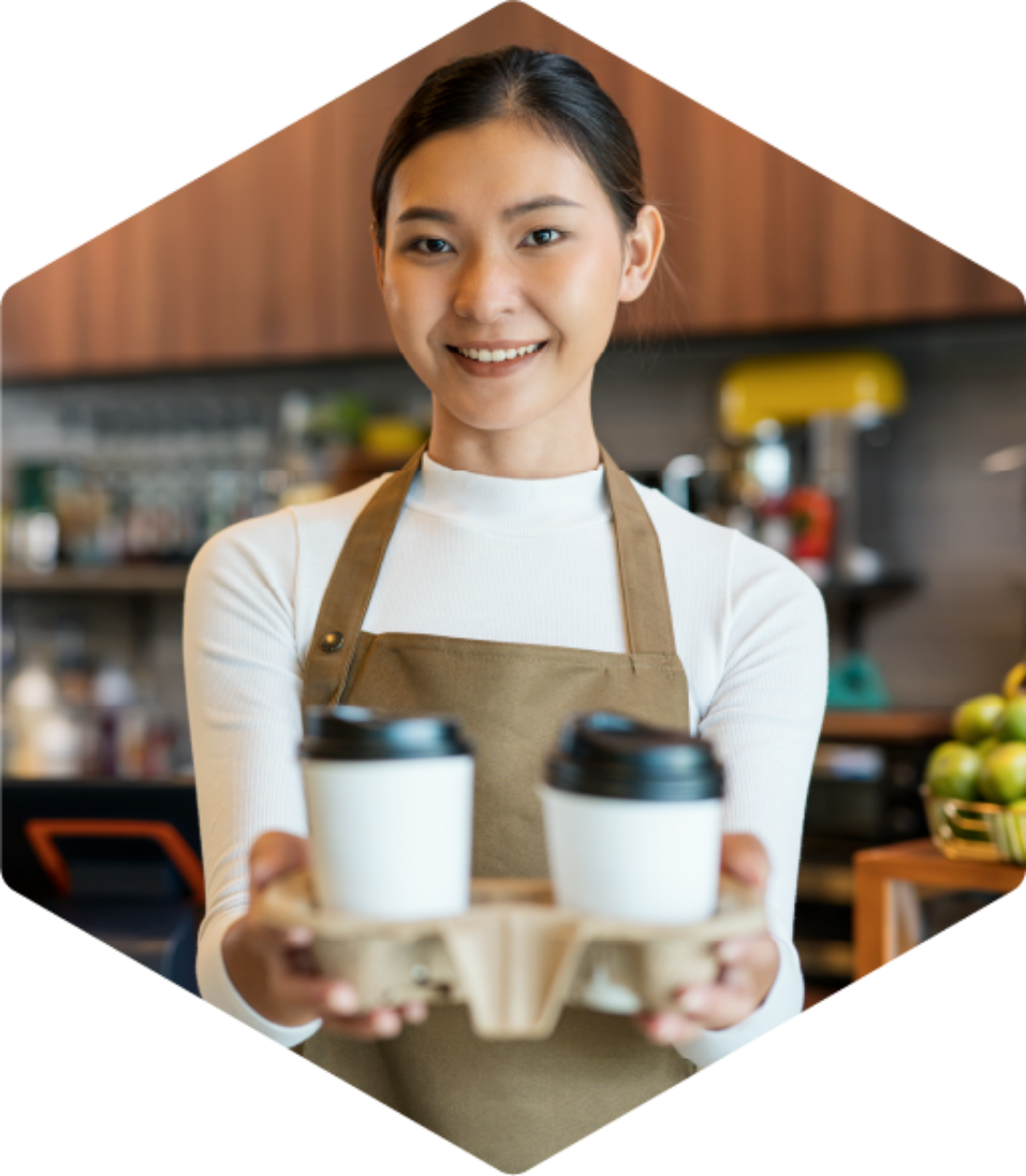 Female barista smiling holding two compostable coffee cups