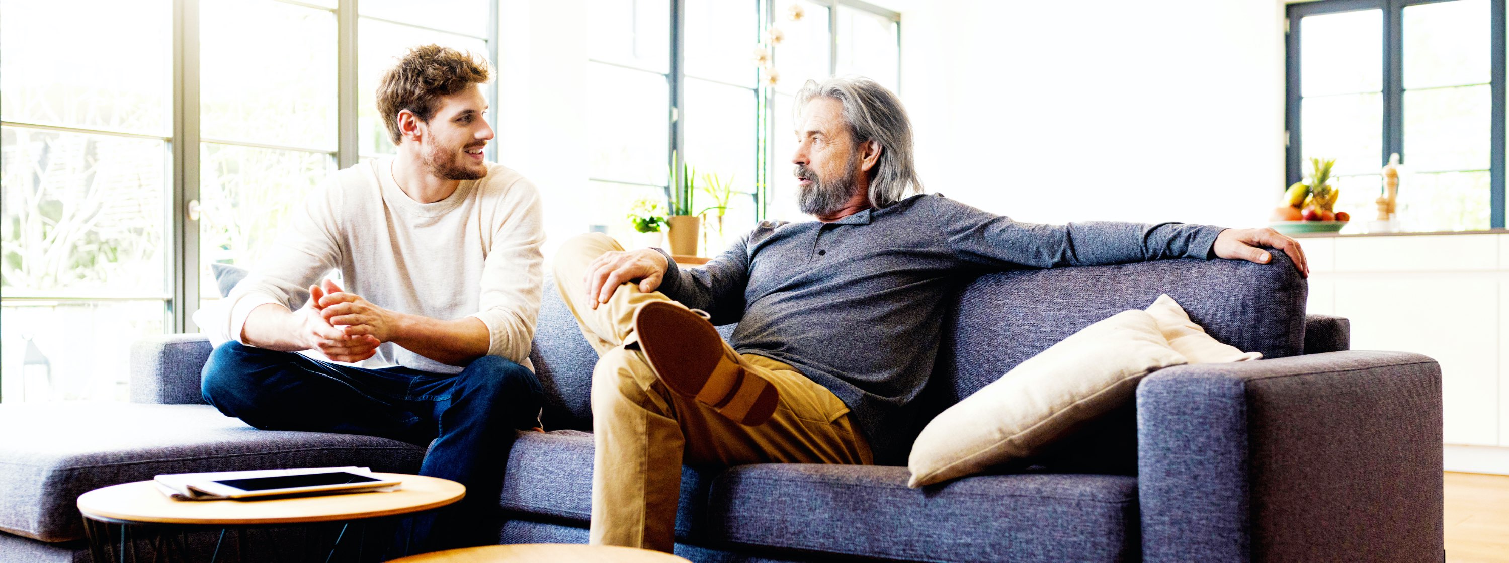 A father and his adult son sit on a couch, talking
