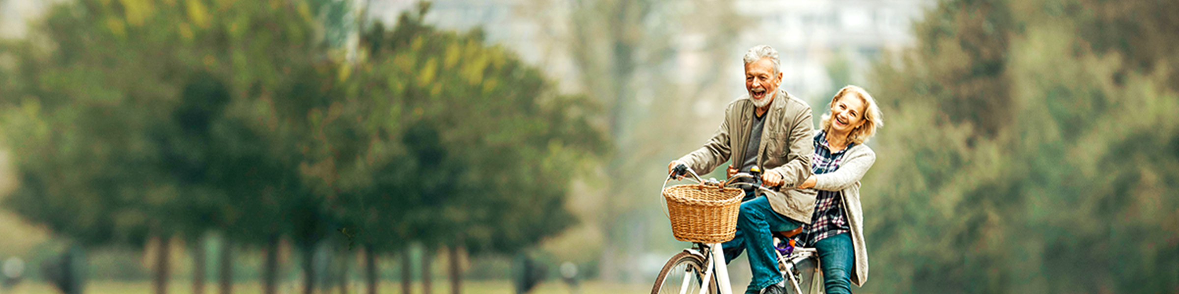 Smiling older couple ride a bike together in a vineyard