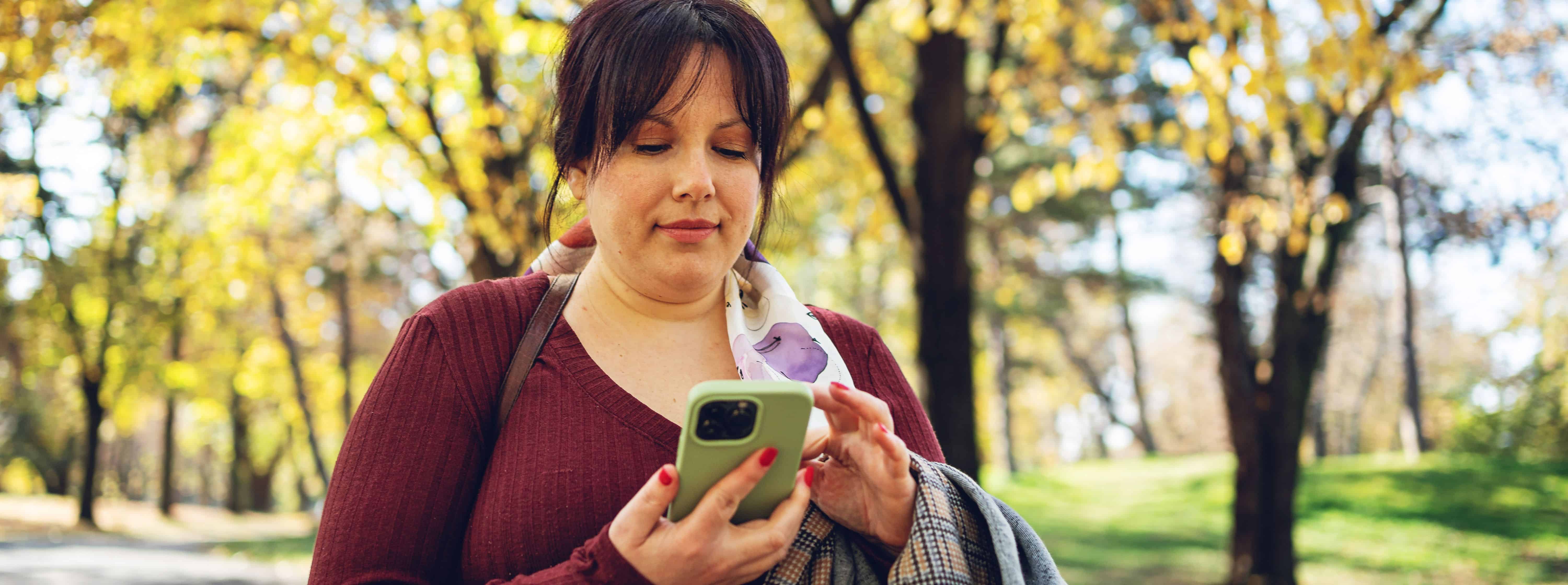 A woman with dark hair in a sweater using a smartphone in the park