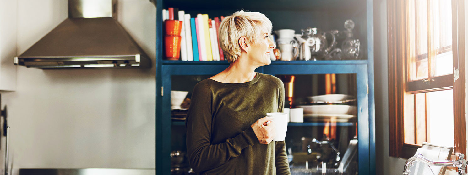 blonde woman holding a coffee cup looking out her kitchen window