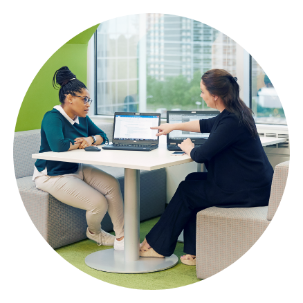 Two female employees sitting together and talking with a laptop open