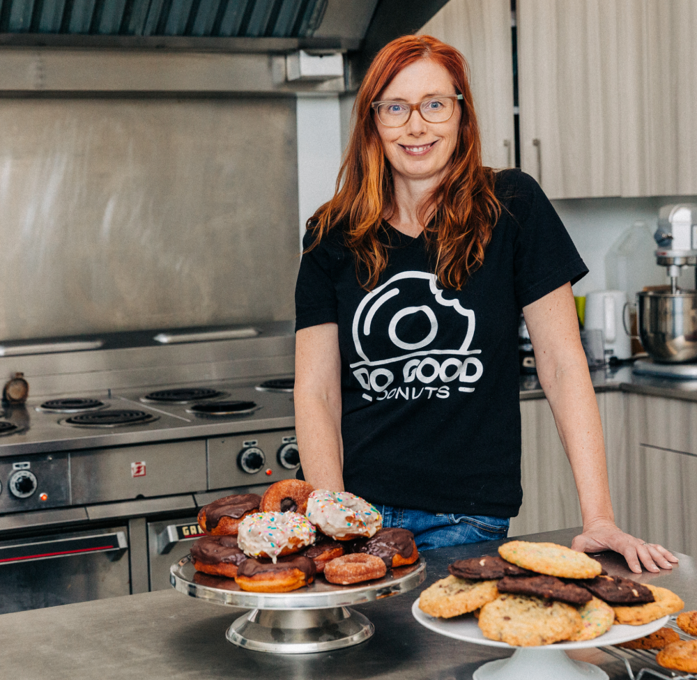 Melanie Côté, founder of Do Good Donuts, stands in a bakery kitchen with a plate of donuts.