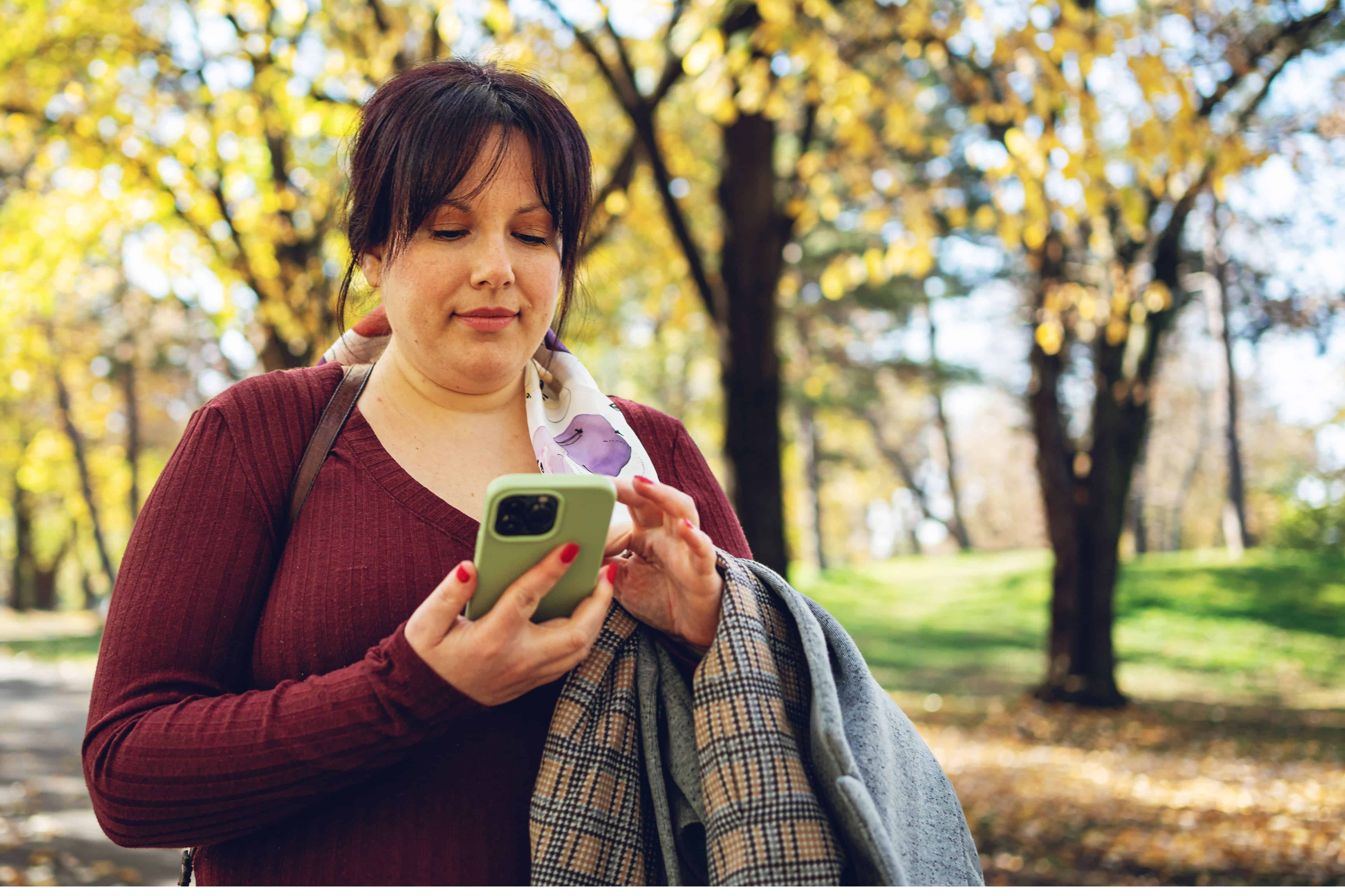 A woman with dark hair in a sweater using a smartphone in the park