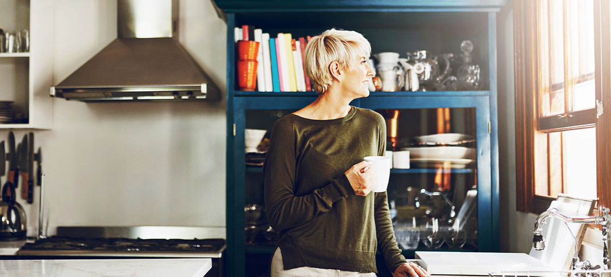 blonde woman holding a coffee cup looking out her kitchen window