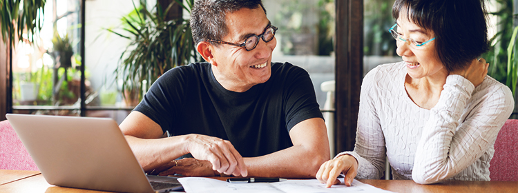 Smiling couple, sitting next to a lap top and reviewing documents