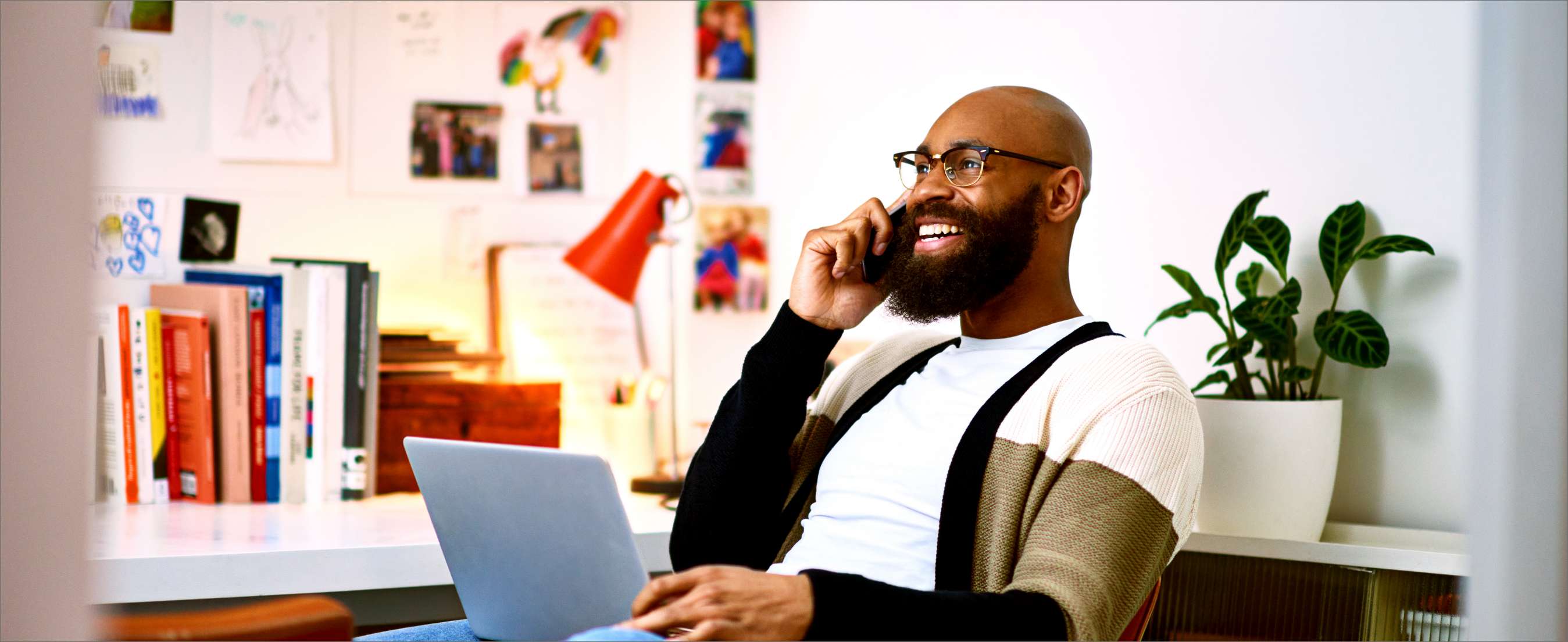 Black man in his 30s sitting on chair with laptop, on phone call.
