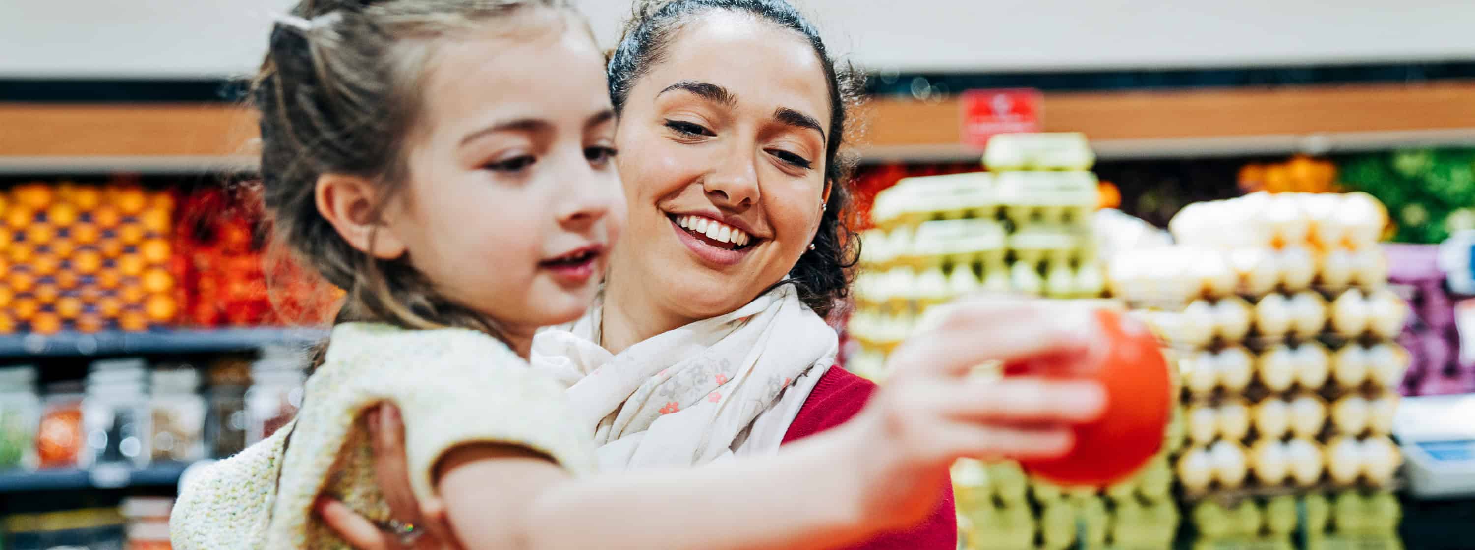 A girl eating an apple on her mother's lap at a grocery store