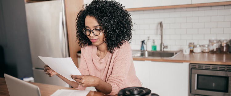 Woman in her kitchen, thoughtfully reviewing documents