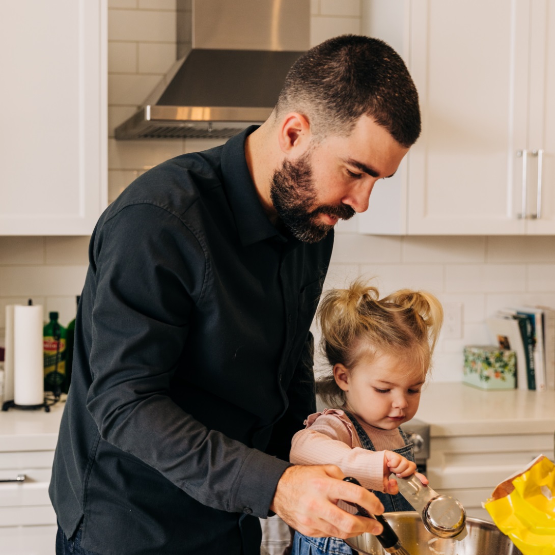 A man and his young daughter cook together in a kitchen.