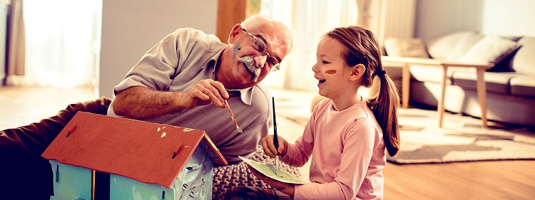 Smiling older man paints a doll house with his granddaughter