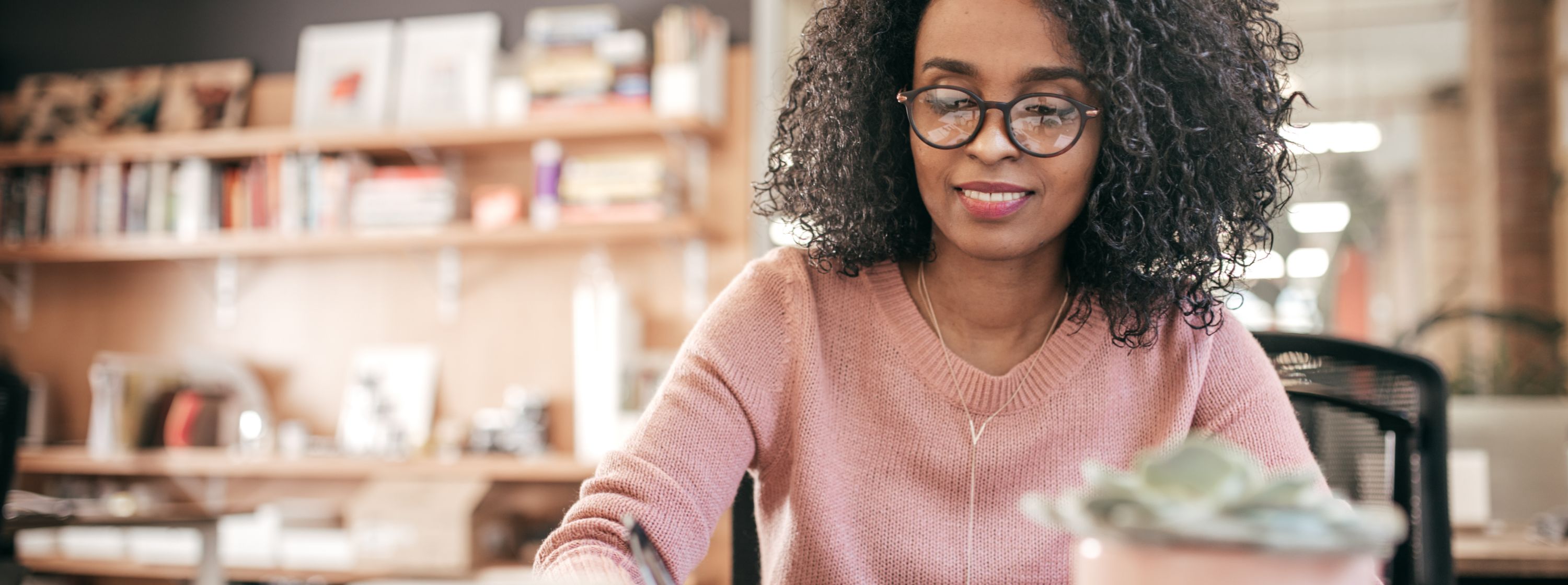 Close up image of woman smiling, wearing glasses, writing in her notebook