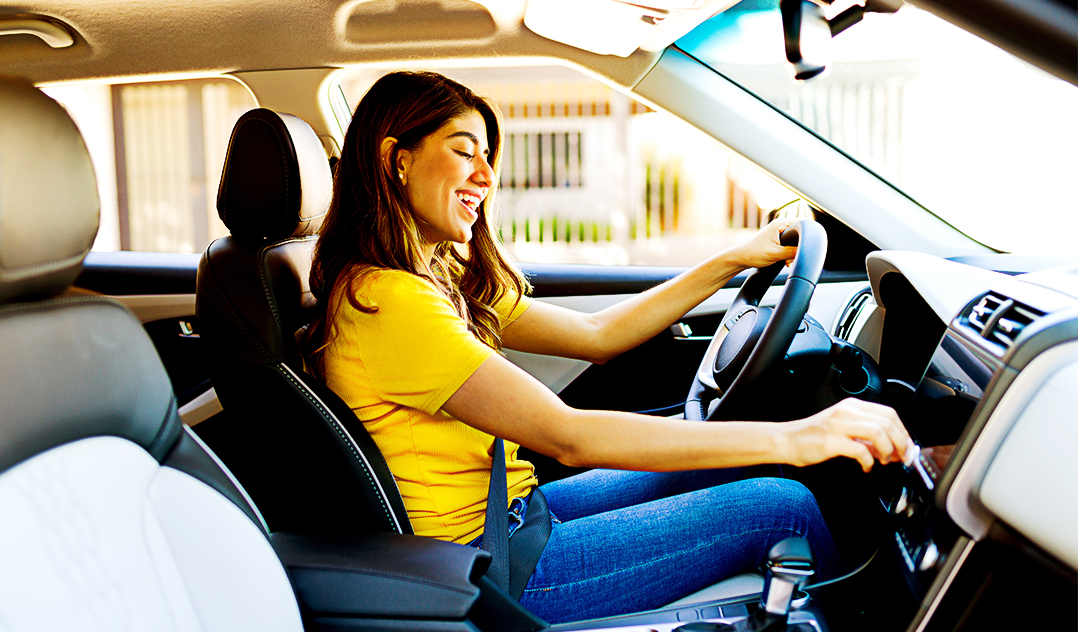 A smiling young women sits in the driver's seat of her car