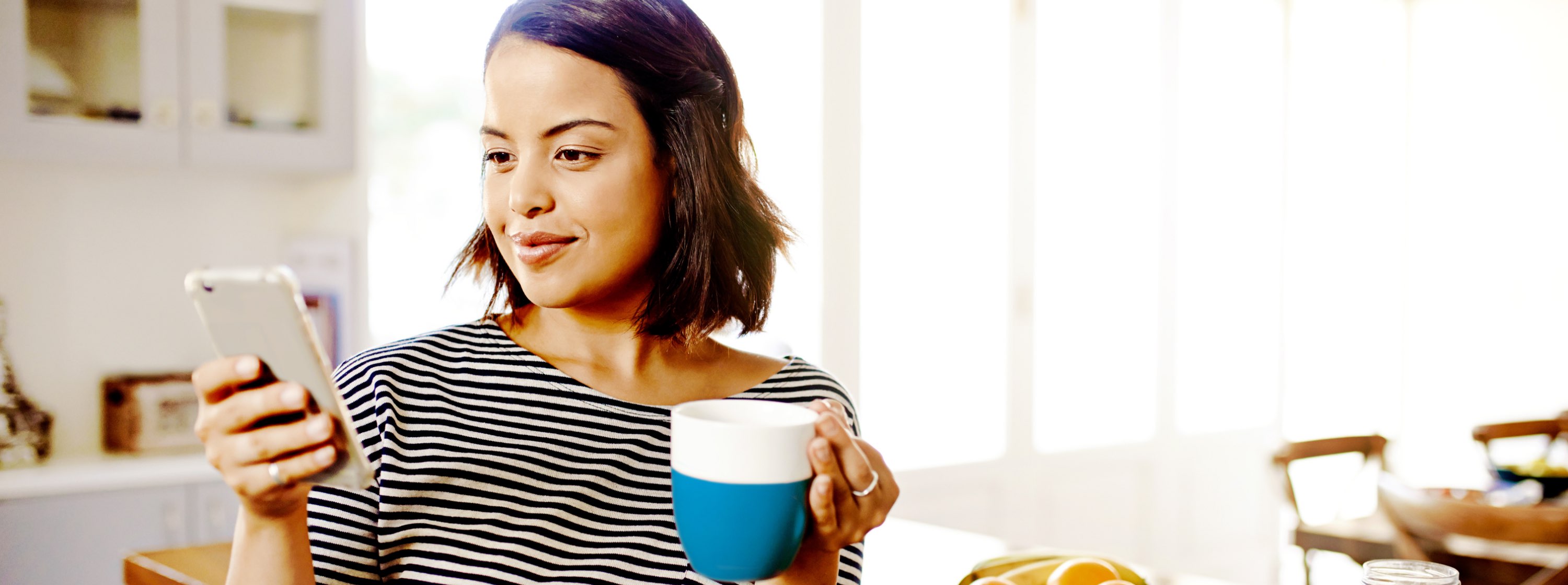 Smiling young woman, looking at her phone and holding coffee