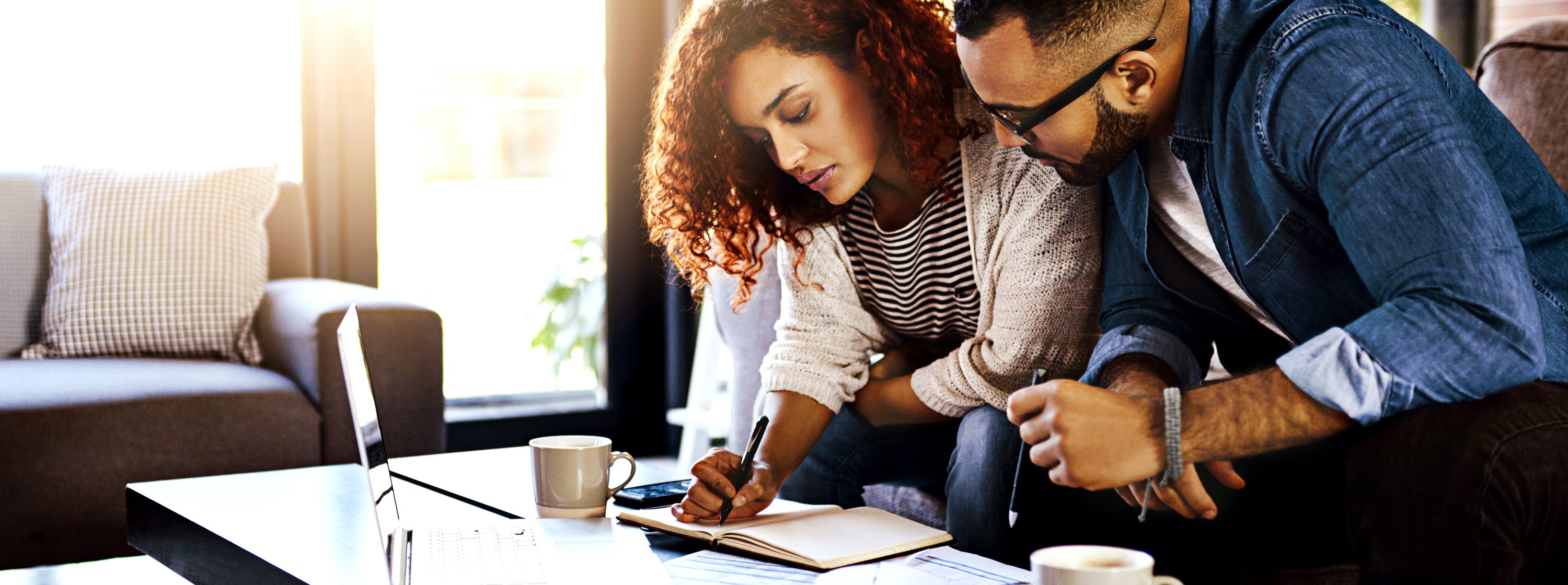 A couple sit at a coffee table, making notes in a journal