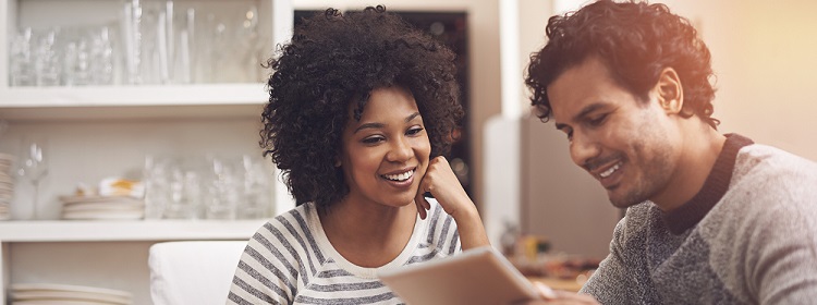 Smiling young couple in their kitchen, reviewing their finances on a laptop