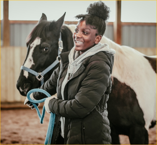A smiling young black woman leading a black and white horse.