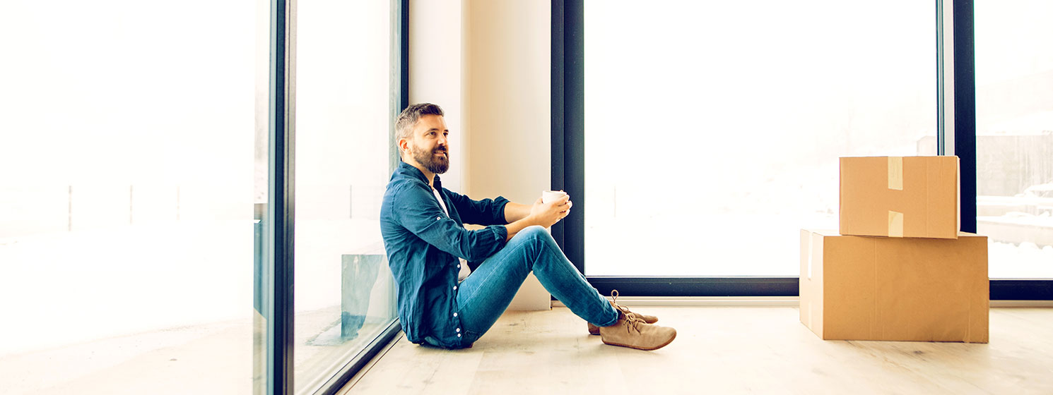 A happy man sitting on the floor of his new home surrounded by boxes